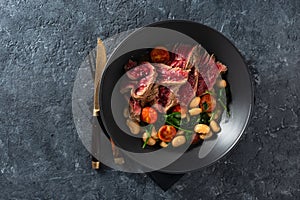 Dinner plate with beef steak with white beans, spinach and tomatoes dark stone background top view with free co