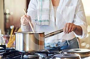 Dinner is almost ready. Cropped shot of a young woman stirring a pot in her kitchen at home.