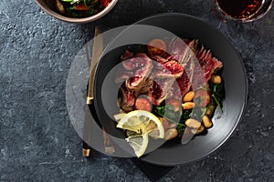 Dinner table. Beef steak with white beans, spinach and tomatoes on dark stone background with glass red wine top view with free