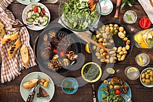 Dinner table with grilled steak, vegetables, potatoes, salad, sn