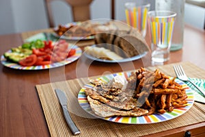 Dinner table with salad dish, chicken, sweet potatoes, bread and colorful water glass