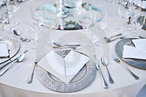 Dinner table setting with stainless plate, fork, spoon and napkin with water glasses in closeup