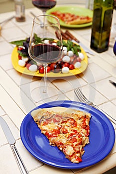 Dinner table. A slice of pizza on a plate and a glass of wine on the table.