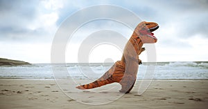 Dinosaur costume, beach and funny with sunshine, comic and running with waves and sand. Blue sky, Halloween outfit and