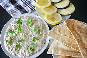 Dip Baba ghanoush with pita bread and fresh lemon on dark wooden table.