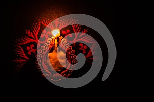 Dipawali Concept - top-view of a glowing Earthen Lamp over a Rangoli design on a black surface with copy space on the right