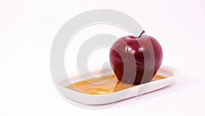 Dipping apple slice in honey on white plate with honey and red apple isolated on a white background
