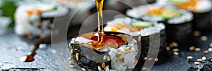 Dipping hosomaki sushi in soy sauce on natural black slate plate background with selective focus photo
