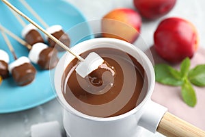 Dipping marshmallow into fondue  with milk chocolate on light table, closeup
