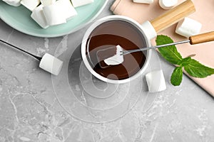 Dipping marshmallow into fondue pot with dark chocolate on marble table