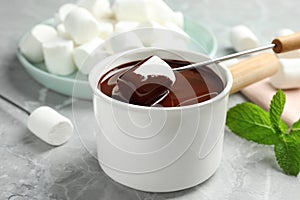 Dipping marshmallow into fondue pot with dark chocolate on marble table