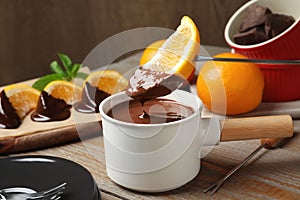 Dipping slice of orange into fondue pot with chocolate on wooden table