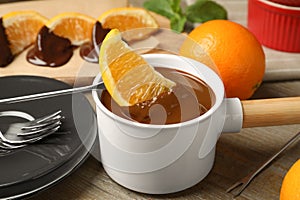 Dipping slice of orange into fondue pot with milk  on wooden table, closeup