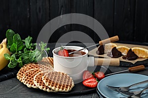 Dipping strawberry into fondue pot with  chocolate on grey table against black wooden background