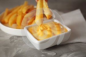 Dipping tasty fries into cheese sauce in bowl