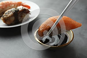 Dipping tasty nigiri sushi with salmon into soy sauce on grey table, closeup