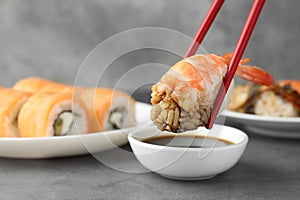 Dipping tasty nigiri sushi with shrimp into soy sauce on grey table, closeup