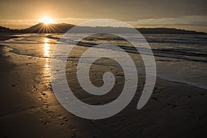 Direct golden sunset`s sunlight on a scenic sandy beach in hendaye in dramatic cloudy atmosphere, basque country, france