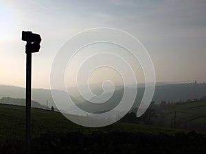 Direction sign in silhouette over misty landscape at daybreak with mist covered hills and valley just before sunrise