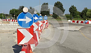 Directional road signs with warning lights on red and white plastic barriers at the edge of a street during roadworks