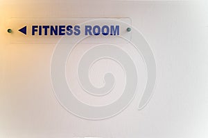 Directional sign to fitness room on white wall.