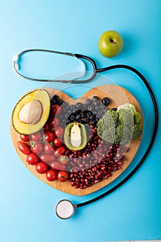 Directly above view of healthy food on heart shaped cutting board by stethoscope on blue background