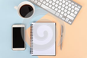 Directly above view of office desk with computer keyboard, cup of coffee,smart phone, note pad and pen on multi colored background photo