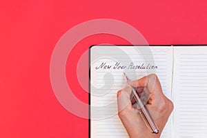 Directly above view of woman`s hand writing words New Year Resolution in a notepad on red background