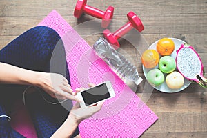 Directly above of woman in fitness clothing using mobile phone with sport equipments and fruits on the floor, Healthy