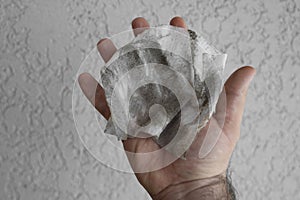 dirt, hairs and grey dust on wet wipes in male hand.  on white wall background