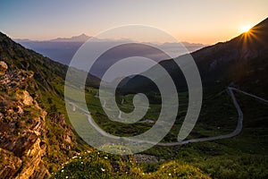 Dirt mountain road leading to high mountain pass in Italy Colle delle Finestre. Expasive view at sunset, colorful dramatic sky,