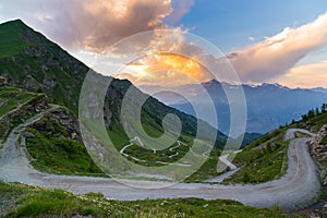 Dirt mountain road leading to high mountain pass in Italy Colle delle Finestre. Expasive view at sunset, colorful dramatic sky,