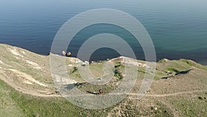 Dirt mountain road runs along hillside along sea. Man rides bike in road