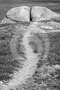 Dirt path leading to a large boulder in open field