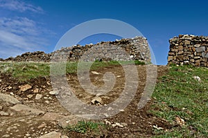 Dirt path leading up to a hole in a drystone wall with clear blue sky in the background
