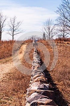 A dirt path walkway next to a stone wall leading up to a military monument on the Gettysburg National Military Park
