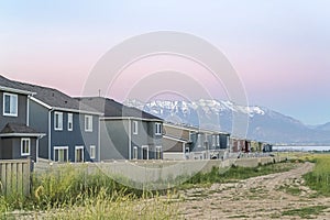 Dirt road along white fences of houses against snow capped mountain at sunset