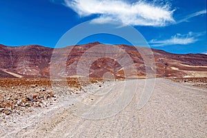 Dirt road in arid barren dry landscape, red mountains, clear blue sky - Road trip to Punta de Jandia, Fuerteventura