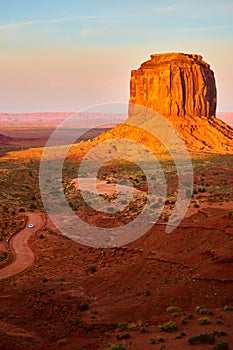 Dirt road with car next to large red rock pillar red in Monument Valley sunset