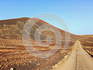Dirt road in desert landscape with volcano on the horizon under blue sky. Nature and extreme sports