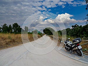 Dirt road with dry yellow vegetation and green trees, with a motorcycle parked