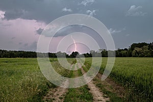 Dirt road through green field and dark stormy sky with clouds