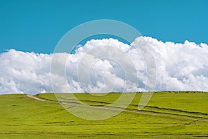 Dirt road through green field and fluffy clouds over hill. Plateau Assy, Kazakhstan
