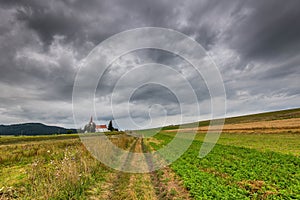 Dirt road leading to a small catholic church through agricultural field