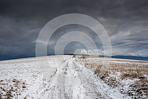 Dirt road leading to the top of the hill at wintertime, dramatic storm clouds