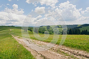 Dirt road on mountains under blue sky. Rural landscape with clouds