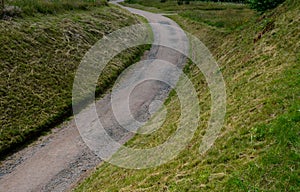 Dirt road in the park gravel beige in the valley somewhere  is a lawn cut low elsewhere is a meadow cutting slopes