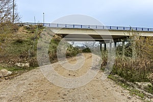 A dirt road passing under a highway bridge with two independent carriageways with circular concrete pillars