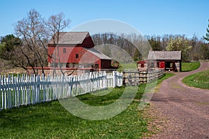 Dirt road with picket fence and a colonial American red barn and log cabin