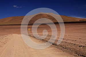 Dirt road through red wasteland contrasting with deep blue cloudless sky,  lost yellow sign showing left direction -